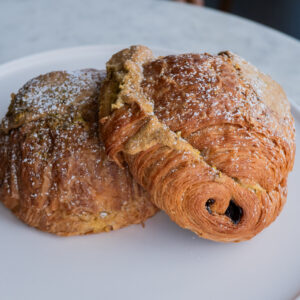 The JL chocolate pistachio croissant is our classic chocolate croissant that has been double-baked with house-made pistachio paste and chopped pistachios. Once baked, we sprinkle powdered sugar on top. Baked fresh daily.